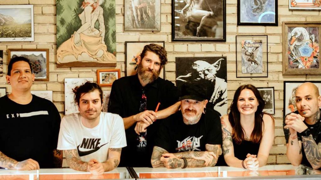 The San Marcos Tattoo Emporium team poses in front of a wall covered with art.